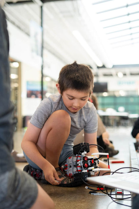 Young boy working on a robot with various parts in a classroom setting