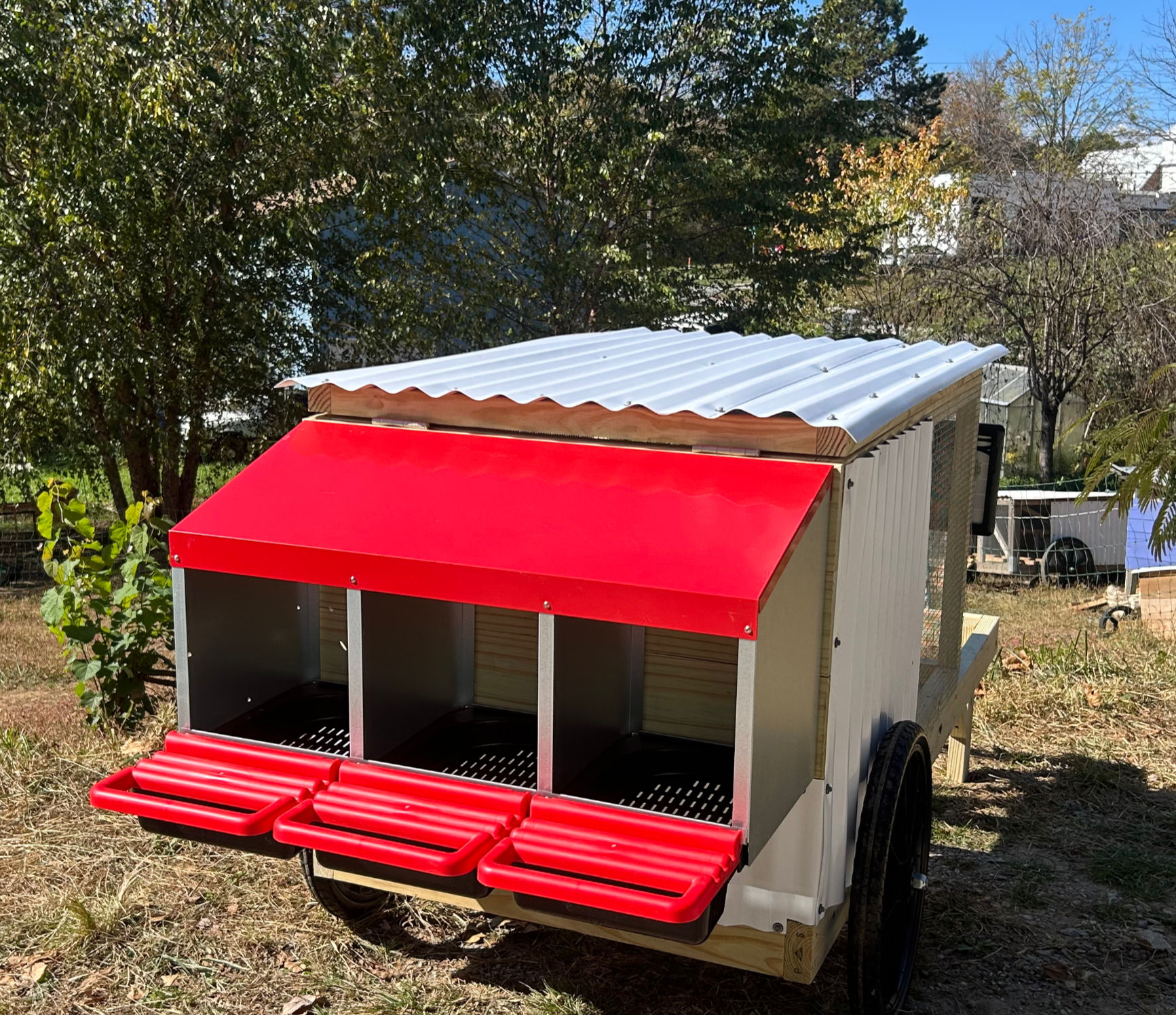 Three red and silver roll-out next boxes on the back of a wheeled chicken coop.