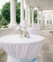 Cocktail table decorated with a small white floral arrangement, greenery, and simple wedding decor.
