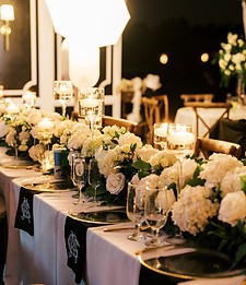 Elegant wedding reception table with floral centerpieces, candles, greenery, and gold place settings.