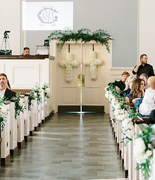 Wedding ceremony aisle lined with white floral arrangements and greenery