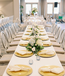 Long wedding reception table with place settings, greenery, candles, and floral accents.