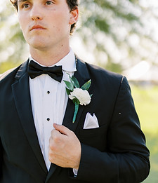 Groom boutonniere with white flowers and greenery pinned to a black suit jacket.