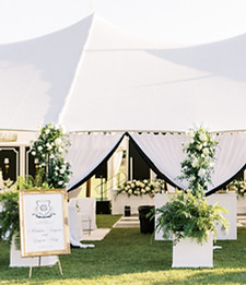 Outdoor tent wedding reception with floral arrangements, greenery, and elegant table decor.