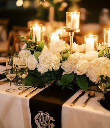 Wedding reception table setting with floral centerpiece, candles, greenery, and elegant place settings.