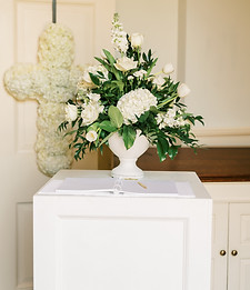 Guest sign-in table with a white floral arrangement, greenery, and wedding decor accents.