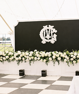 Black floral backdrop with custom monogram, white flowers, and greenery for weddings and special events.