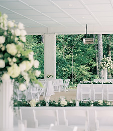Wedding reception table with white floral centerpieces, greenery, candles, and elegant table settings.