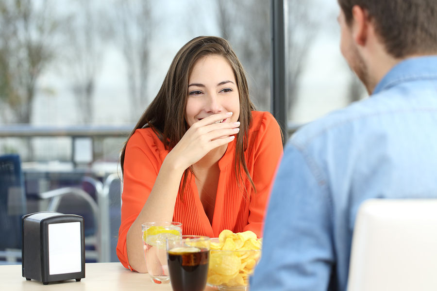 Woman covering her mouth to hide bad breath during a date in a coffee shop