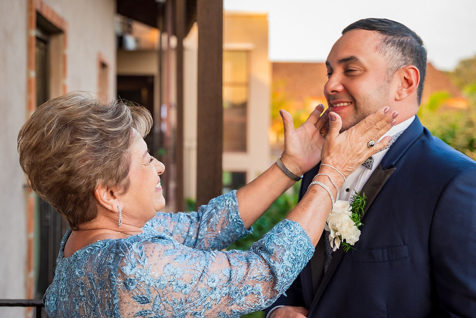 Mamá del novio y novio de perfil en el balcón del Hotel Cubitá, mientras ella le acaricia las mejillas con ambas manos y ambos se sonríen en un momento tierno antes de la ceremonia de boda en Azuero, Panamá. Ciudad de Panamá. Fotografía por Ahmed Saturno.