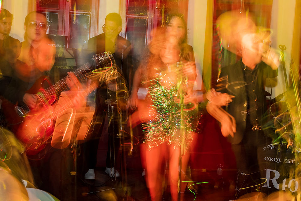 Banda de música tocando en la recepción de boda con un efecto shutter drag que deja ver el movimiento de las luces y de los músicos en escena, creando una sensación dinámica y festiva mientras ambientan la celebración de los novios. Ciudad de Panamá. Fotografía por Ahmed Saturno.