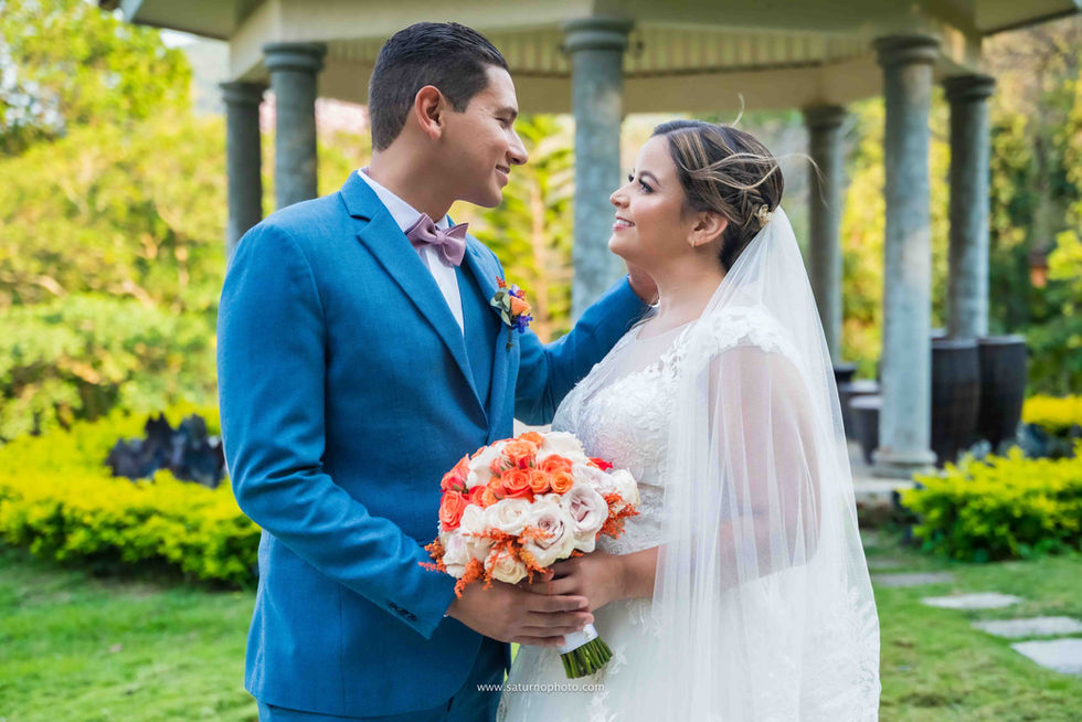 Retrato medium shot de los novios en Casa Lourdes; el novio a la izquierda y la novia a la derecha se miran de forma tierna frente a frente mientras él le acaricia el rostro con su mano izquierda, rodeados de la naturaleza de El Valle de Antón, Panamá. Fotografía por Ahmed Saturno.