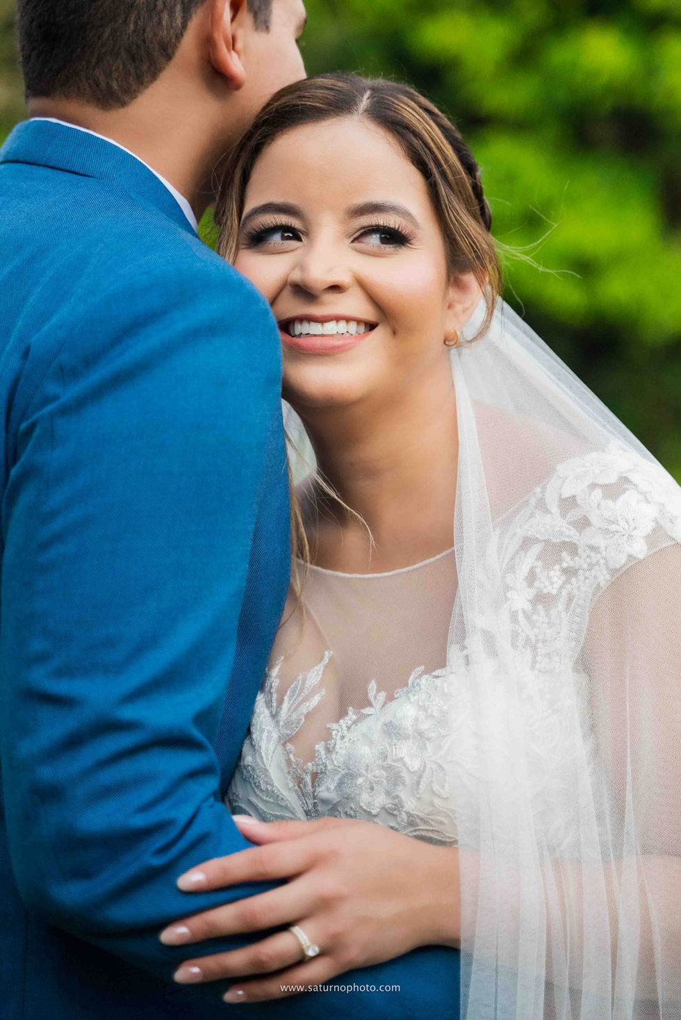 Retrato medium shot del rostro de la novia recostada en el pecho del novio; ella sonríe mientras mira hacia el horizonte y toma su antebrazo, mientras el rostro de él permanece fuera de plano al mirar hacia el fondo en Casa Lourdes, El Valle de Antón, Panamá. Fotografía por Ahmed Saturno.