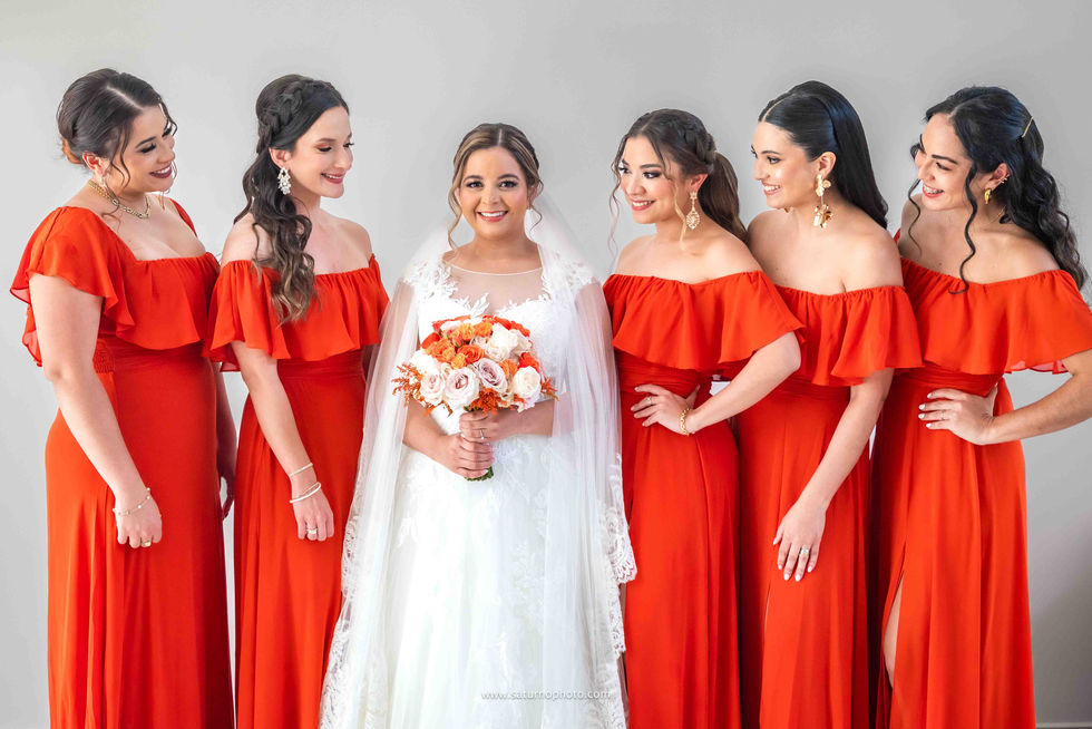 Novia posando sonriente a la cámara sosteniendo su ramo mientras sus cinco damas de honor la miran súper felices a su alrededor, todas ya arregladas en la casa familiar antes de salir hacia la iglesia para la boda en El Valle de Antón, Panamá. Fotografía por Ahmed Saturno.