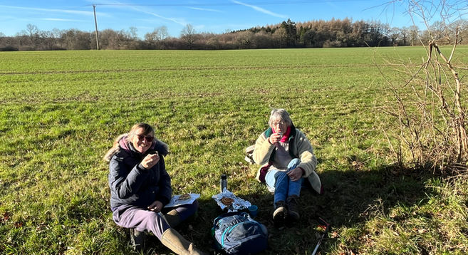 2 walkers on a recce sitting on grass and drinking from a flask at Burridge Heath