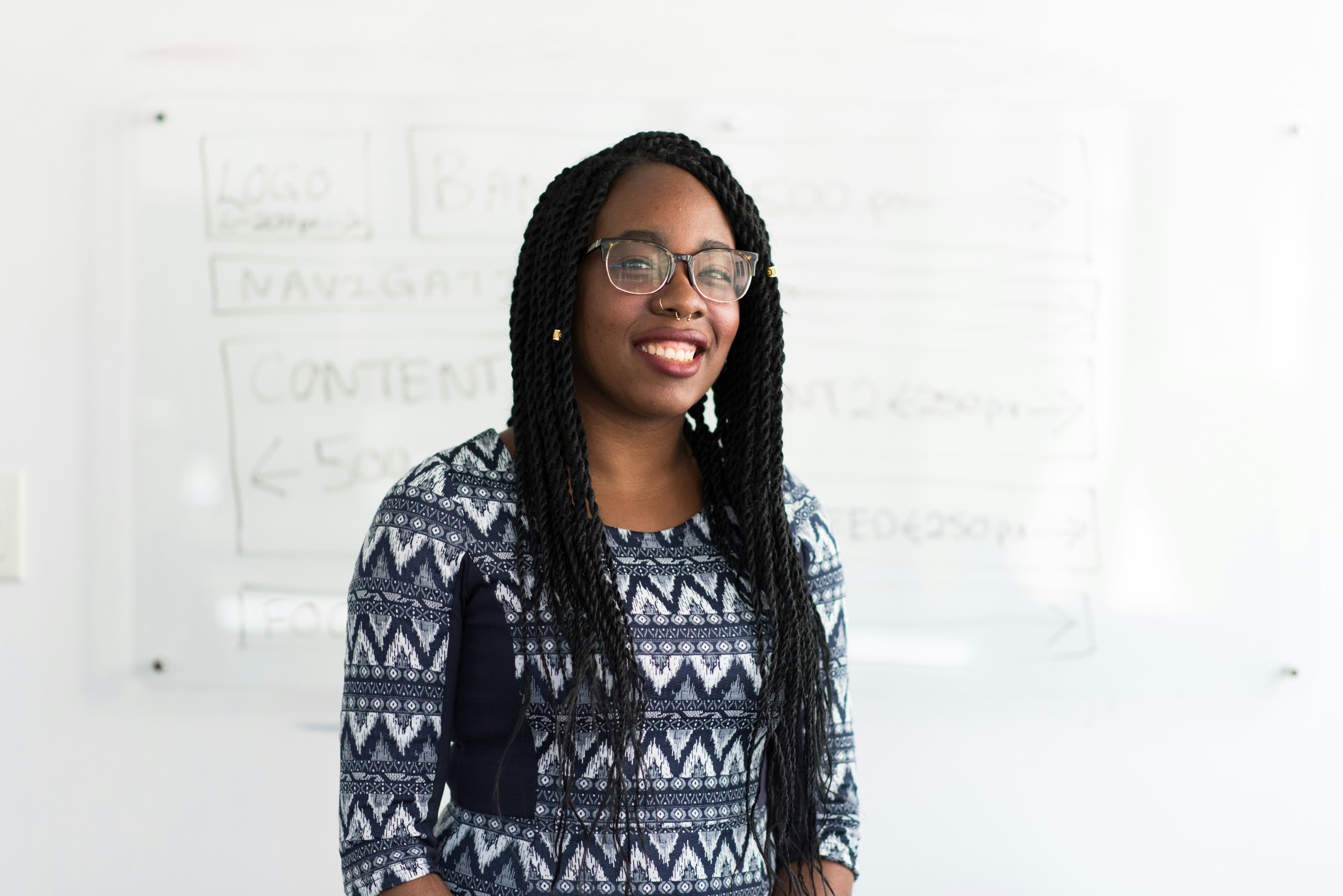 Smiling woman with glasses in front of white board displaying UI elements.