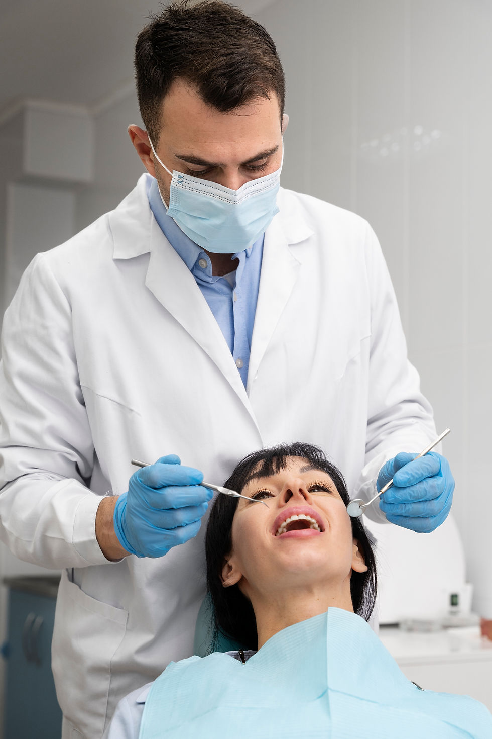 Dentist examining patient's teeth; woman smiles during dental checkup procedure.