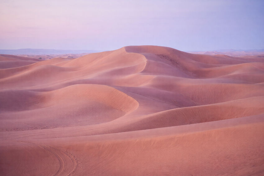 Panorama del desierto de Erg Chegaga con dunas doradas y suaves curvas iluminadas por la luz del amanecer, mostrando la inmensidad y serenidad del Sahara.