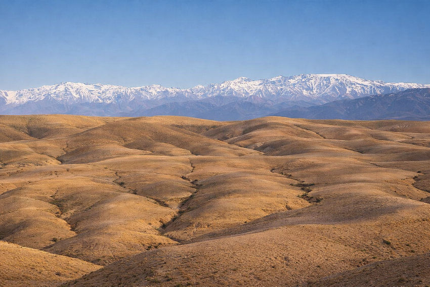 



Paisaje panorámico del Desierto de Agafay cerca de Marrakech, con colinas doradas y los montes Atlas nevados al fondo bajo