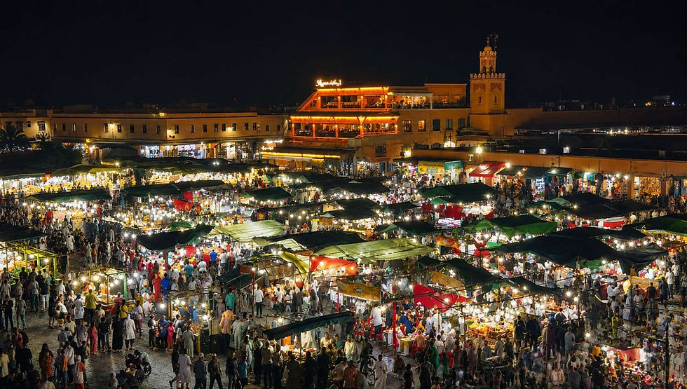 Wide nighttime view of Jemaa el-Fna Square in Marrakech, Morocco, bustling with crowds and colorful market stalls beneath warm lights