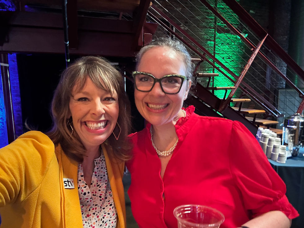 Two women leaning in shoulder to shoulder. Smiling.