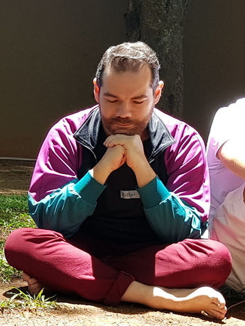 Psicólogo Arthur Ceratti sentado num gramado, em posição pensativa e com as pernas cruzadas