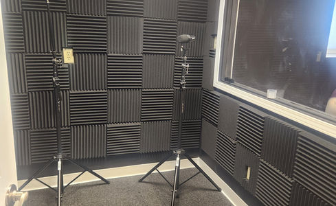 Recording studio with two microphone stands and black soundproofing foam panels.