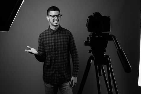 Young man with camera gestures in studio, preparing for filming session.