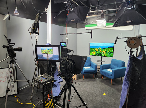 TV studio setup with cameras, monitors, and chairs; green screen background.