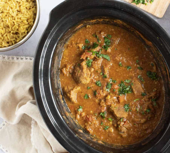 Beef Curry in a black slow cooker with rice on the side