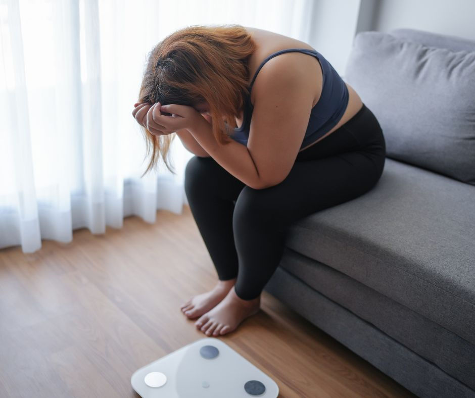 women with head in hands beside weight scales