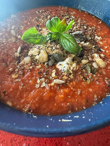 Tomato soup in a blue bowl with seeds and basil on top
