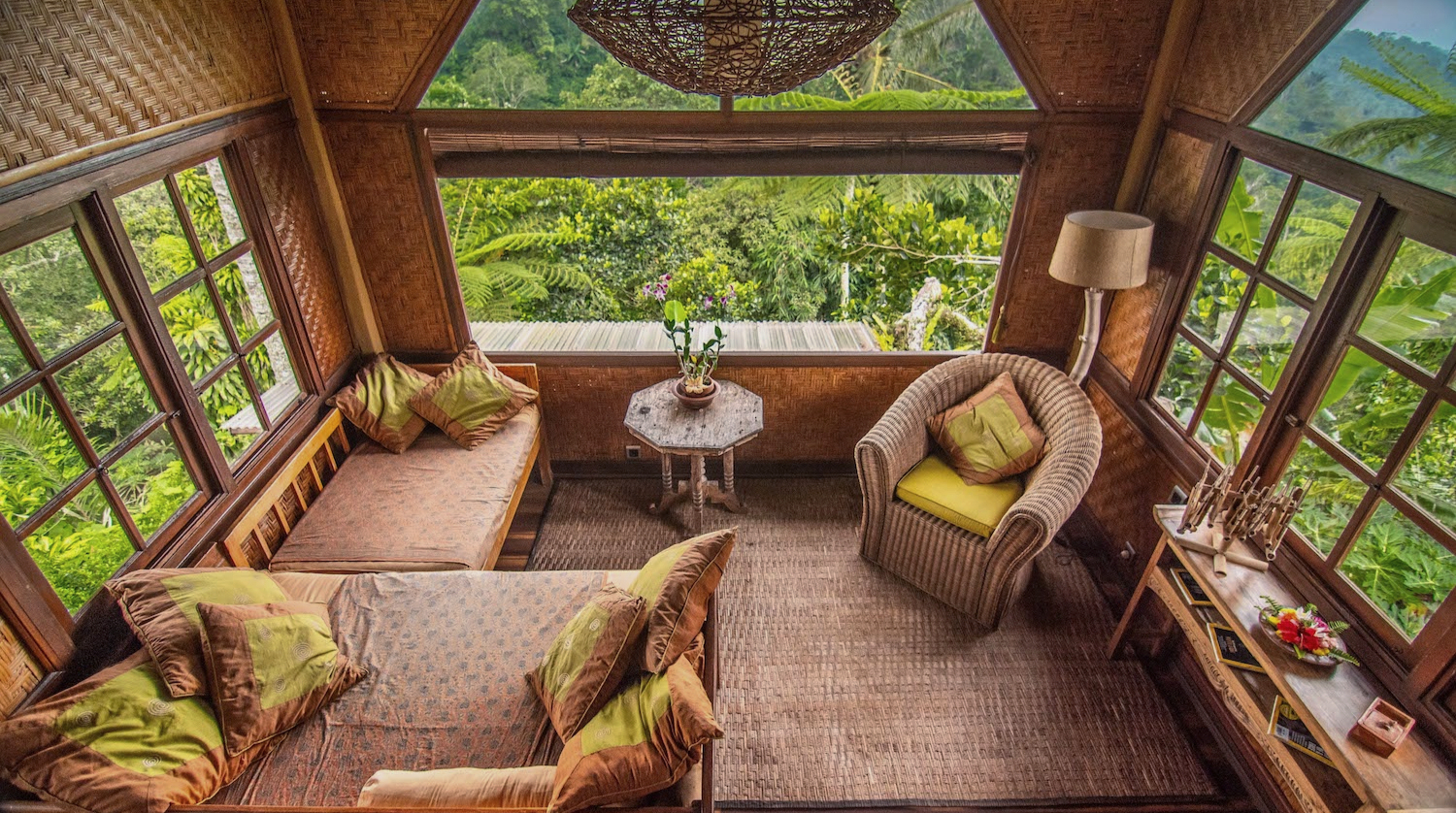 A bungalow lounge with cushioned benches under a bank of timber framed windows, looking out over the garden to the mountain.