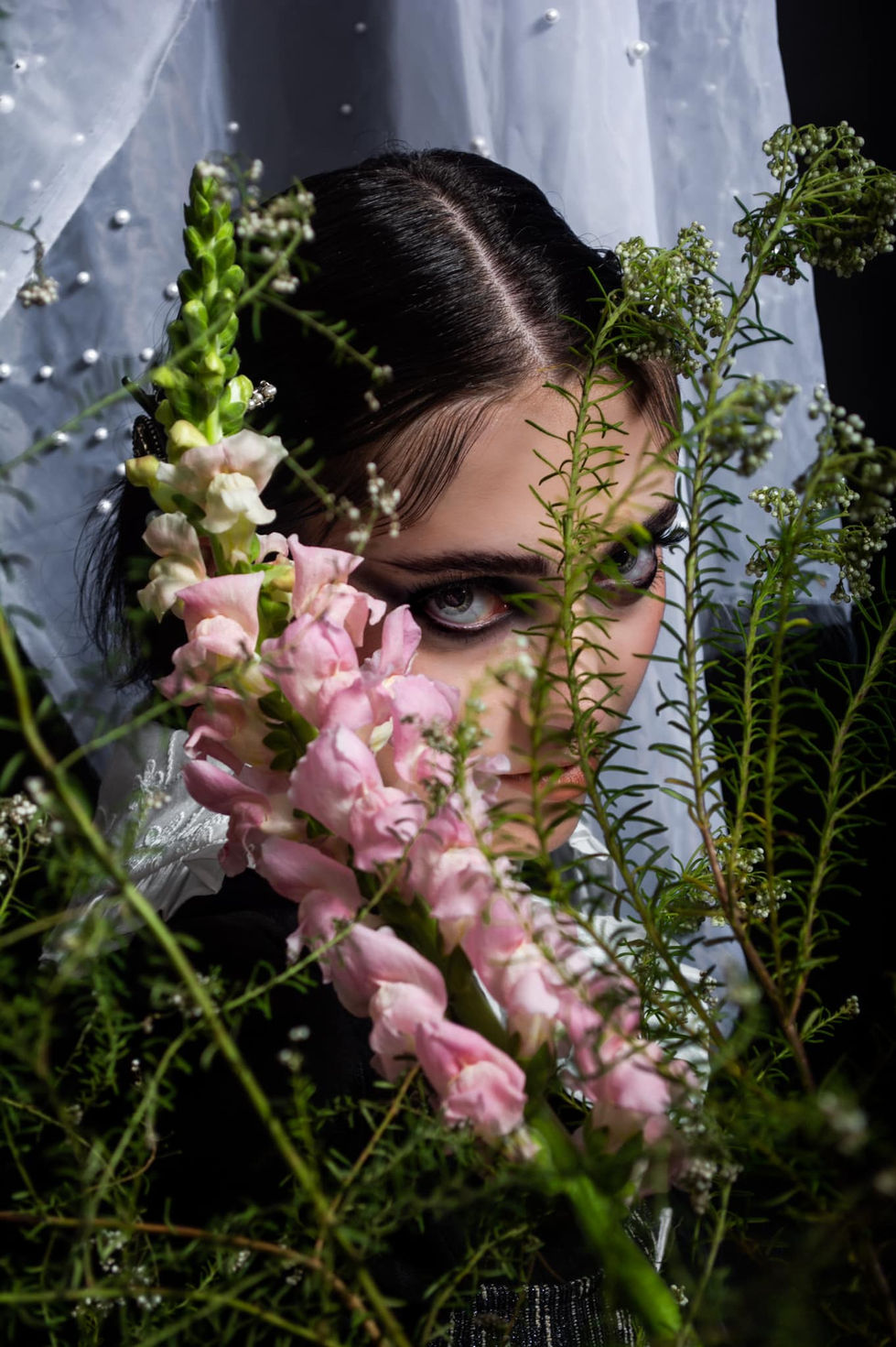 Woman peeking through flowers, intense eyes, Mugshot Makeup Artis, dark background.