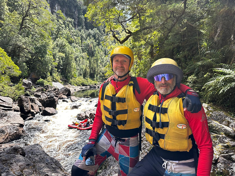 Two men in rafting gear by a rocky river