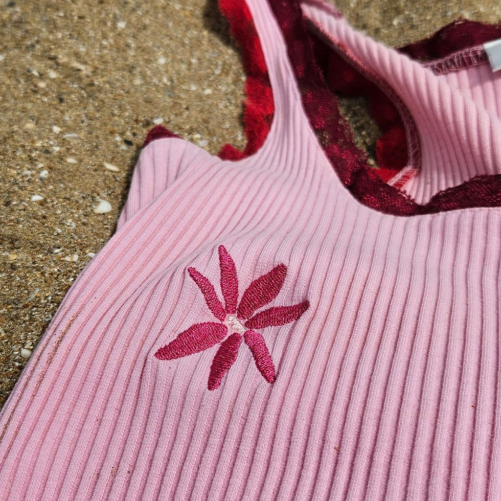 Thumbnail: Close-up of a machine embroidery flower on a pink ribbed tank top laying in the sand.