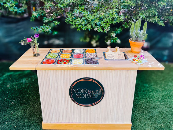 Noir & Nopal charcuterie cart outdoors with colorful toppings display, fresh flowers, and cactus decor.