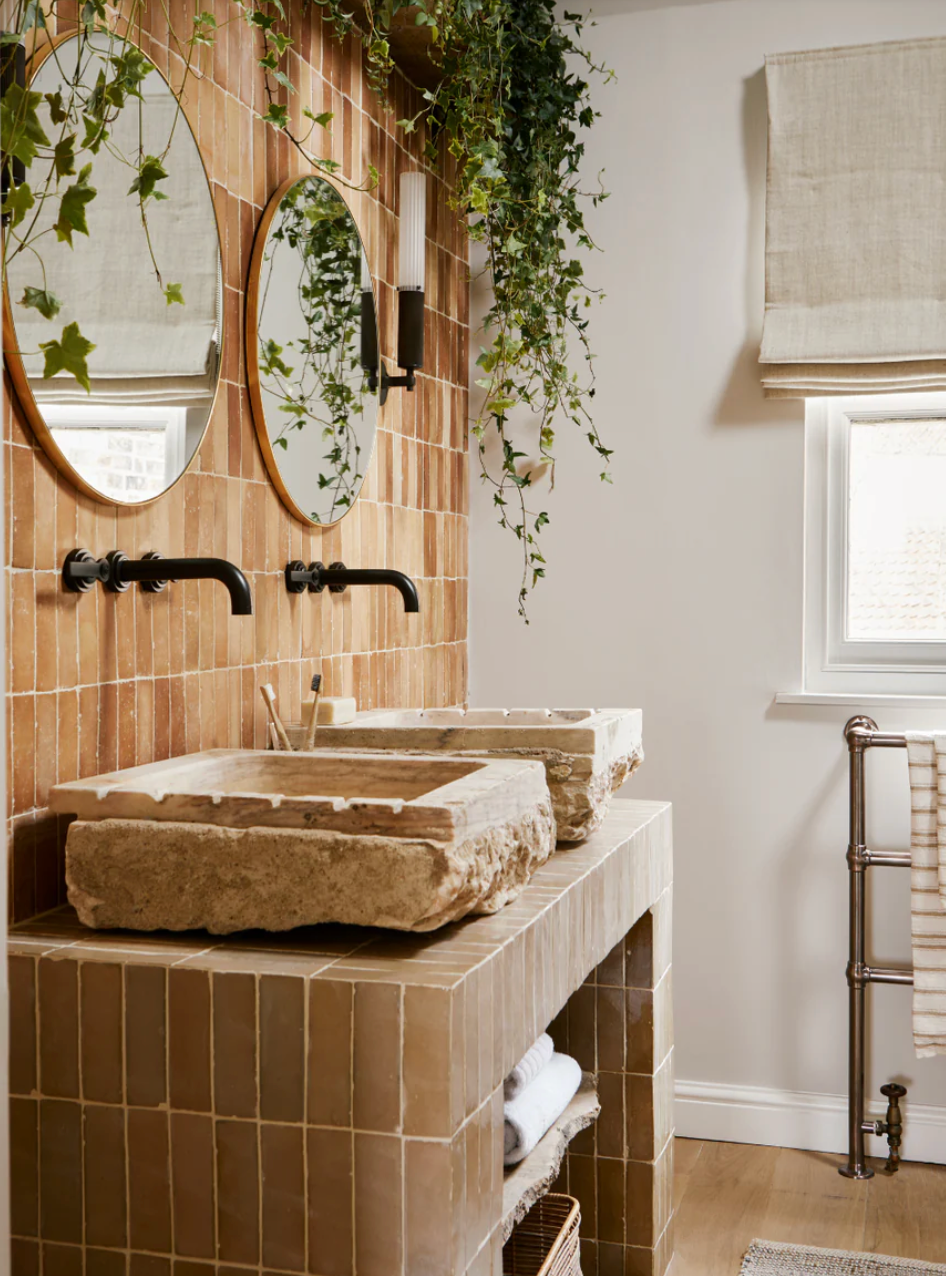 Earthy elegance meets modern design as Bert& May showcase a stunning bathroom with mixed metal accents, stone sinks, and lush greenery for a natural, sophisticated look.