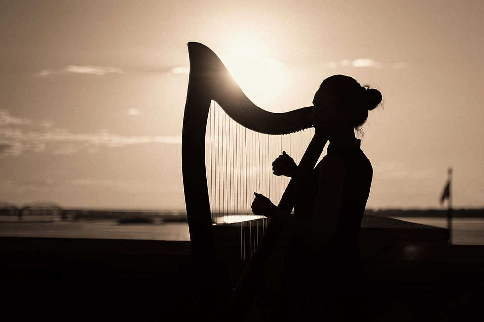 Silhouette d’une harpiste jouant au coucher du soleil au bord de l’eau, dans une ambiance calme et dorée.