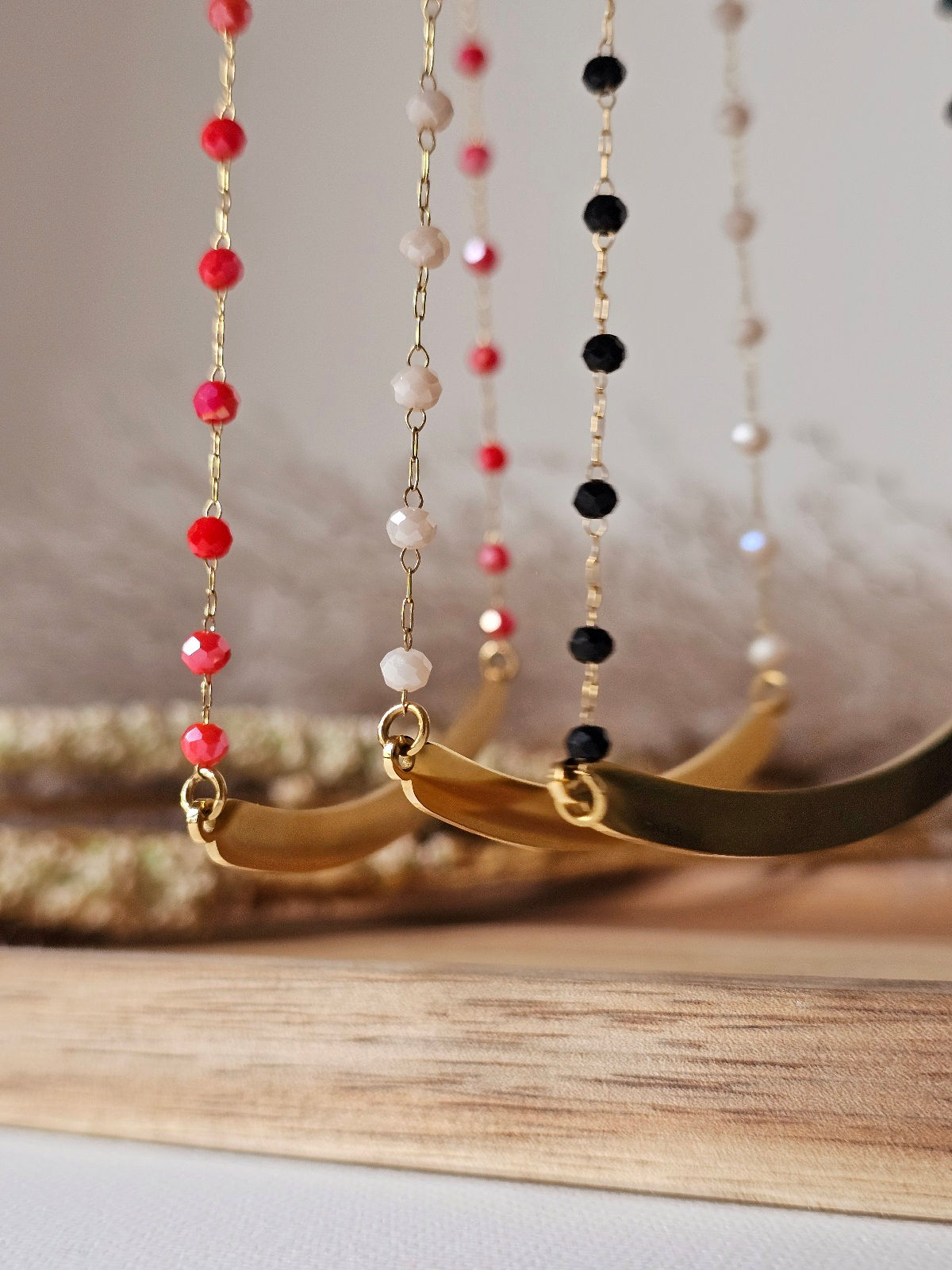 Detailní záběr na tři barevné varianty korálkových řetízků se zlatým středovým komponentem