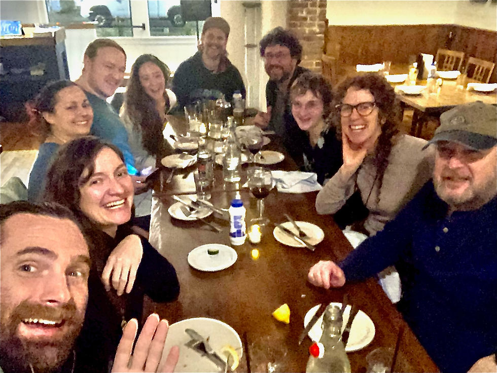 Group of ten people smiling at a restaurant table with drinks, plates, and cutlery, set in a cozy, warmly lit room.