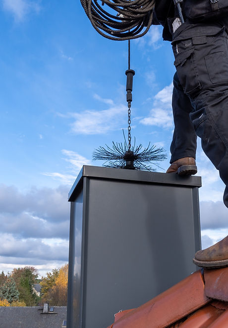 Chimney sweep cleaning a chimney standing on the house roof, lowering equipment down the f