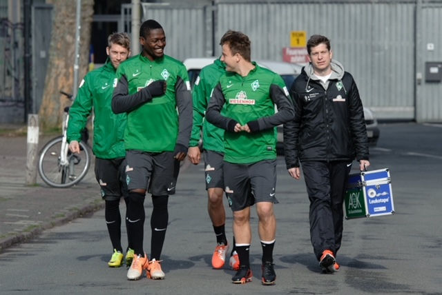 Football players dressed in green and grey training uniform walking with physiotherapist