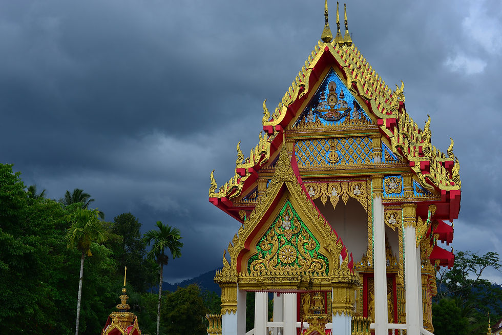 Thailändischer Tempel mit goldenen Verzierungen vor dunklen Regenwolken