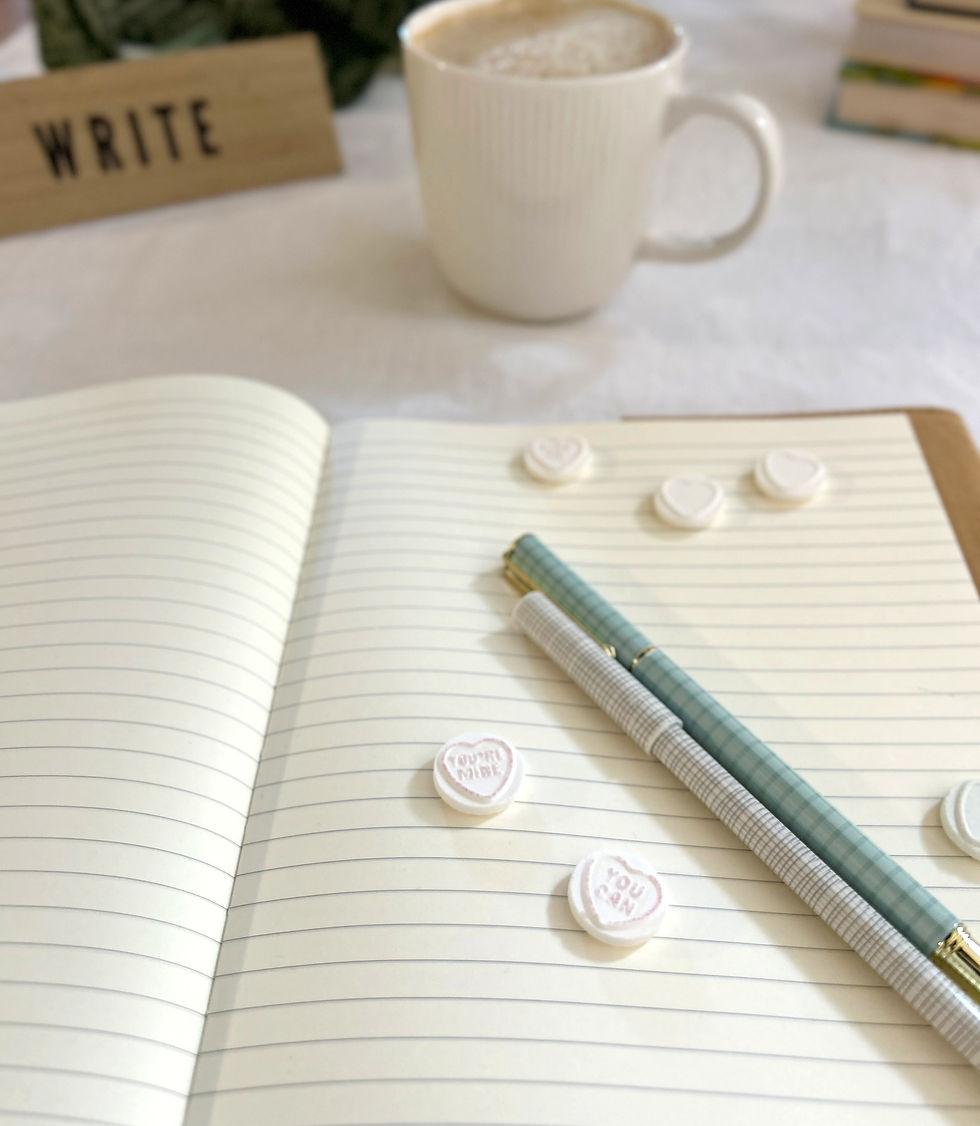 A open notebook with blank lined pages, with two pens resting on top and scattered with candy hearts.