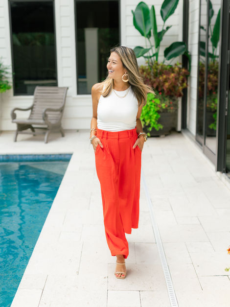 Woman in white halter top, red pants, walking by pool