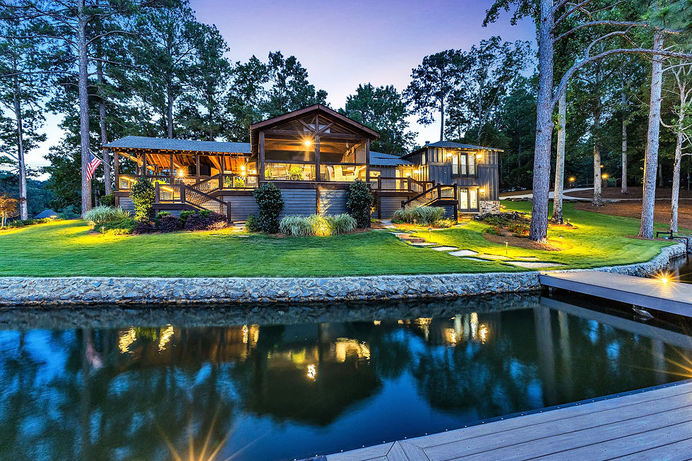 Large house with a deck and dock by a lake at dusk.