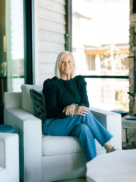 Blonde woman in dark top and jeans seated in armchair