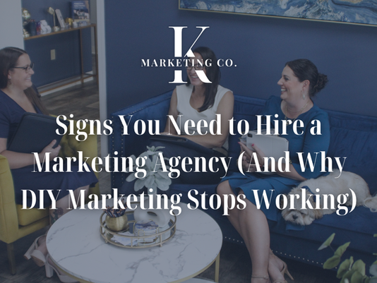 Three women converse in a modern office with blue walls, sitting on a couch and chair. Text reads: "Signs You Need to Hire a Marketing Agency."