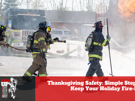 Three firefighters in full turnout gear and air tanks advance a hose line toward a large training fire outdoors while flames rise into the air. A fire engine is parked behind them as water sprays across the scene. A red banner at the bottom reads, “Thanksgiving Safety: Simple Steps to Keep Your Holiday Fire-Free,” alongside a “Step Up” firefighter recruitment graphic.